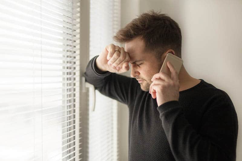 hombre atendiendo una llamada por teléfono junto a la ventana de su casa