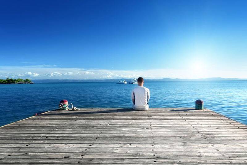 man sitting alone on boat dock in front of sea