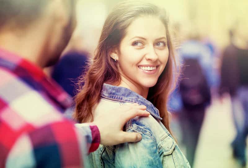 man touches smiling woman shoulder