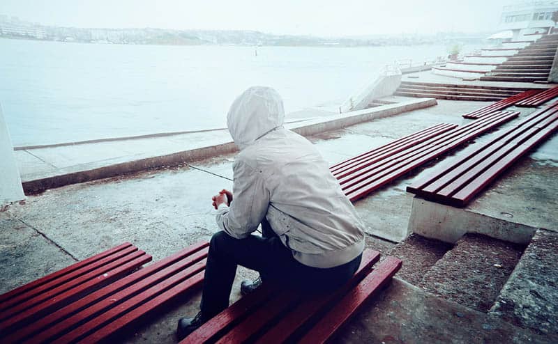 man wearing hoodie sitting beside water