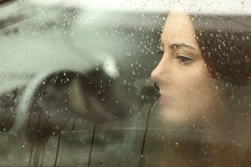sad woman looking through the rainy window