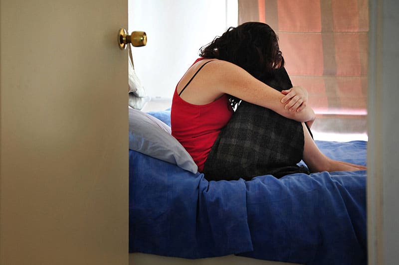 Mujer víctima joven deprimida sentada y llorando en la cama en casa sufriendo de una depresión severa. Foto de concepto de víctima de secuestro, violación y delito 
