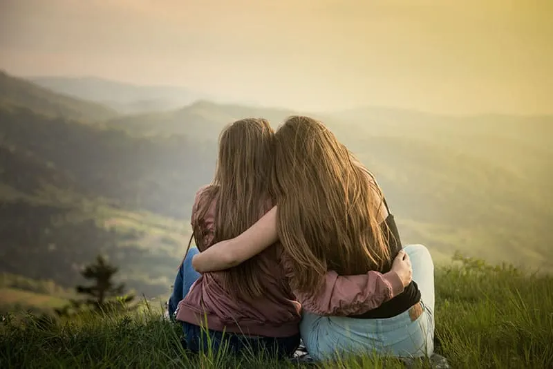 Two friends hugging looking at the Carpathians mountains. Two girls on top of the mountain watching at sunset.