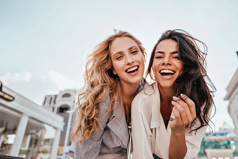 Appealing long-haired girls posing on sky background. Laughing ladies enjoying weekend together