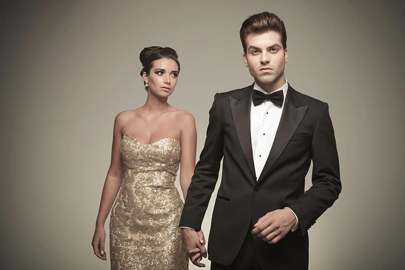 Handsome young elegant man holding his girlfriend by hand while she is looking away from the camera.