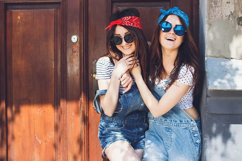eautiful young brunette twins sisters, in stylish sunglasses, hugging and laughing. Having fun time together