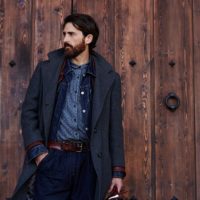 Handsome confident mature man with beard stands on wooden brown background with copy space for your text message or advertising, fashionable rich male dressed in expensive clothes posing outdoors