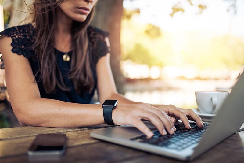 Mujer joven con smartwatch usando ordenador portátil. Mujer que trabaja en la computadora portátil en un café al aire libre.