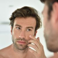 Handsome man applying facial cream in front of mirror