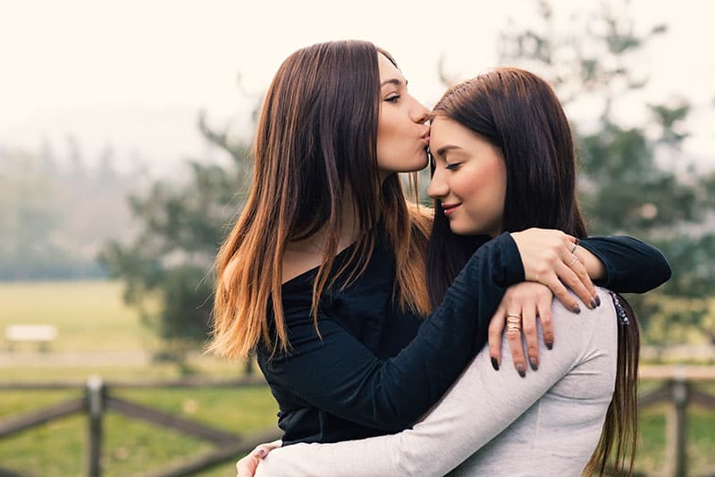Retrato de hermanas jóvenes abrazándose y besándose al aire libre en un parque