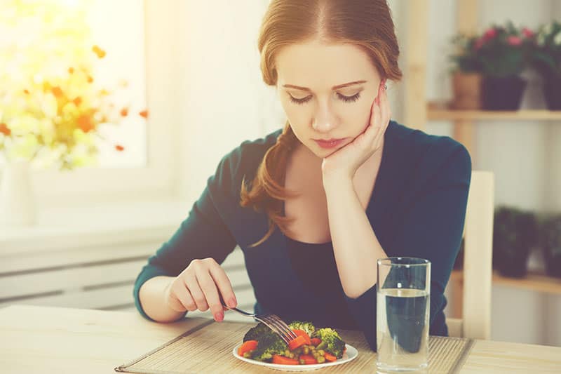 joven mujer triste come verduras en casa en la cocina verano