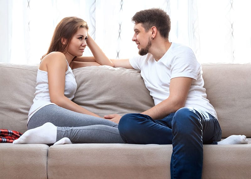 Hombre y mujer joven sentados en un sofá y hablando. 