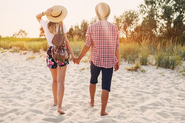 Young hipster couple in love enjoying romantic evening on the beach, holding hands and watching the sunset.
