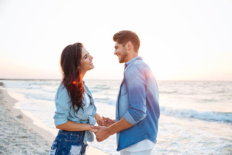 Jovem casal feliz de mãos dadas e a rir na praia