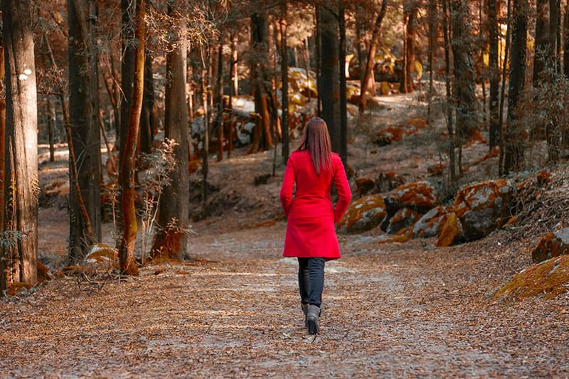 Giovane donna che si allontana da sola su un sentiero forestale indossando un cappotto rosso