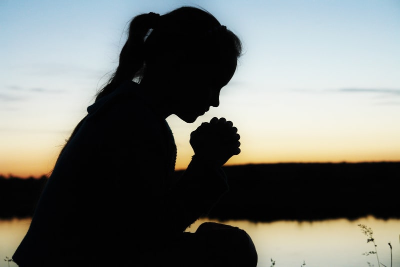 young woman praying in sunset