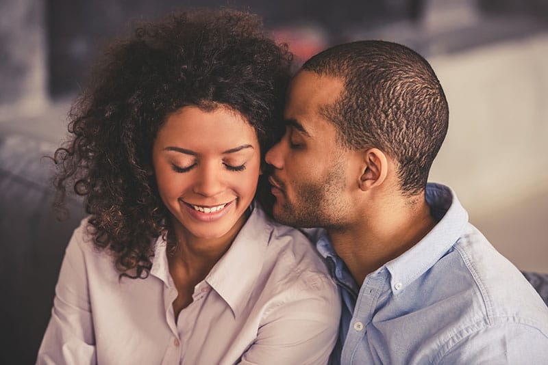 Bella giovane coppia afroamericana si abbraccia e sorride mentre è seduta insieme sul divano di casa