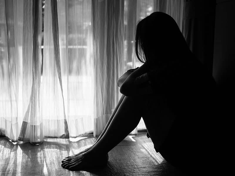 bianco e nero di donna triste abbracciare il suo ginocchio e piangere. Donna triste seduta da sola in una stanza vuota accanto a una finestra o a una porta 