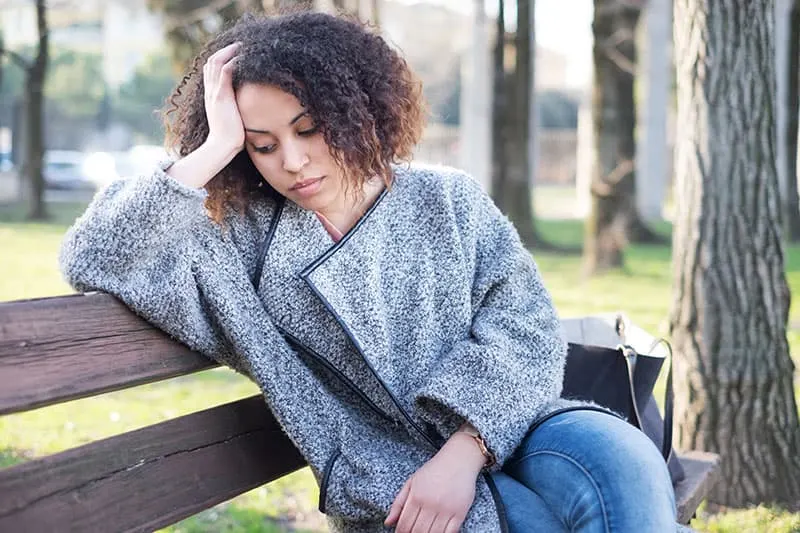Sad black woman seated alone on a bench at the park