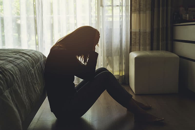 Mujer joven solitaria deprimida y estresada sentada con la cabeza entre las manos en el dormitorio oscuro
