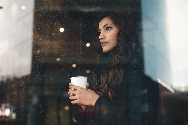 Mujer joven mirando a través de una ventana lluviosa