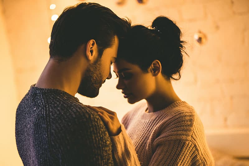 Apasionada pareja romántica en suéteres están pasando tiempo juntos antes de Año Nuevo en casa. Tierna pareja abrazándose sobre el fondo de guirnalda brillante.