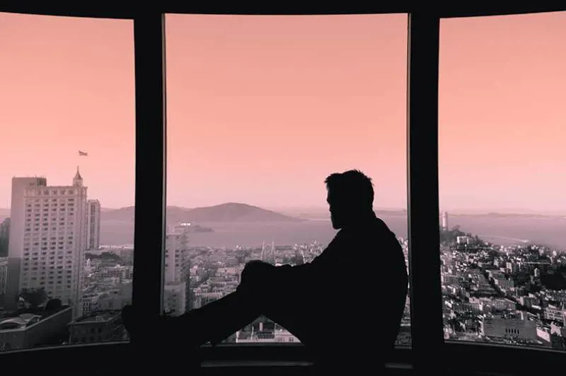 silhouette of man looking on city from window