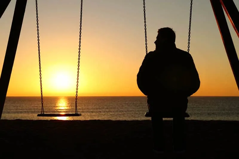 silhouette of man sitting on swing in front of sea