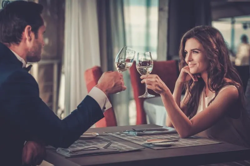 smiling couple looking each other while cheering glass of wine in restaurant