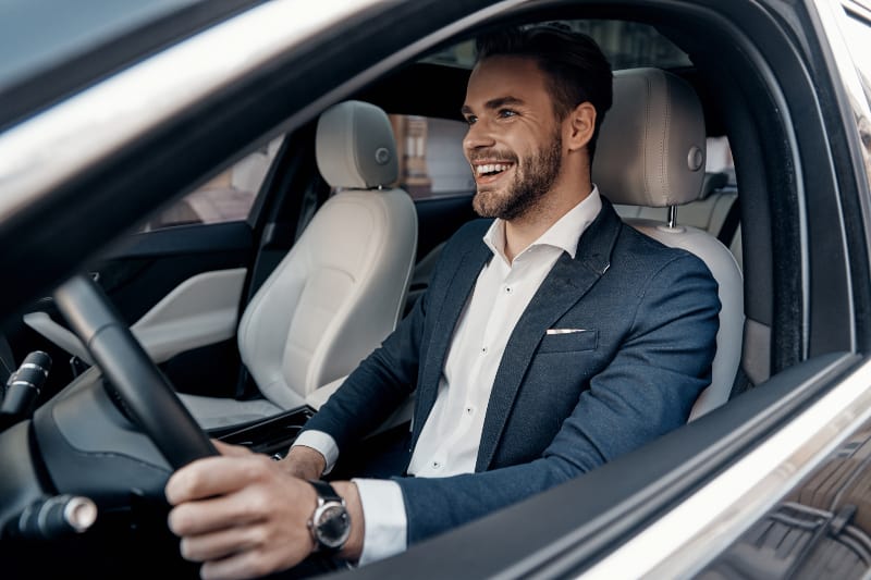 hombre sonriente con traje conduciendo un coche