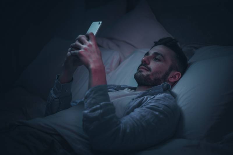 uomo sorridente che usa lo smartphone prima di andare a letto