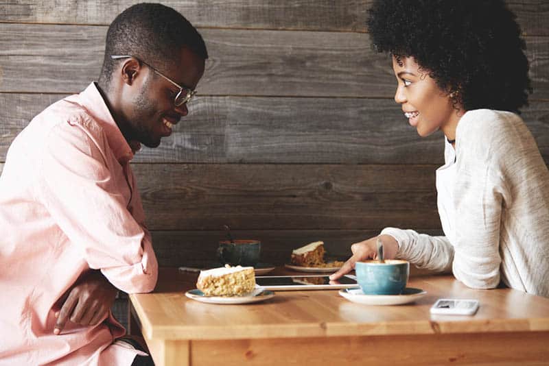 smiling woman pointing on tablet while man looking at in cafe