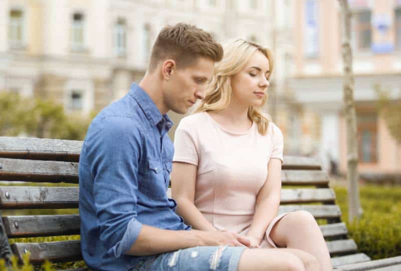 thoughtful couple sitting on park bench