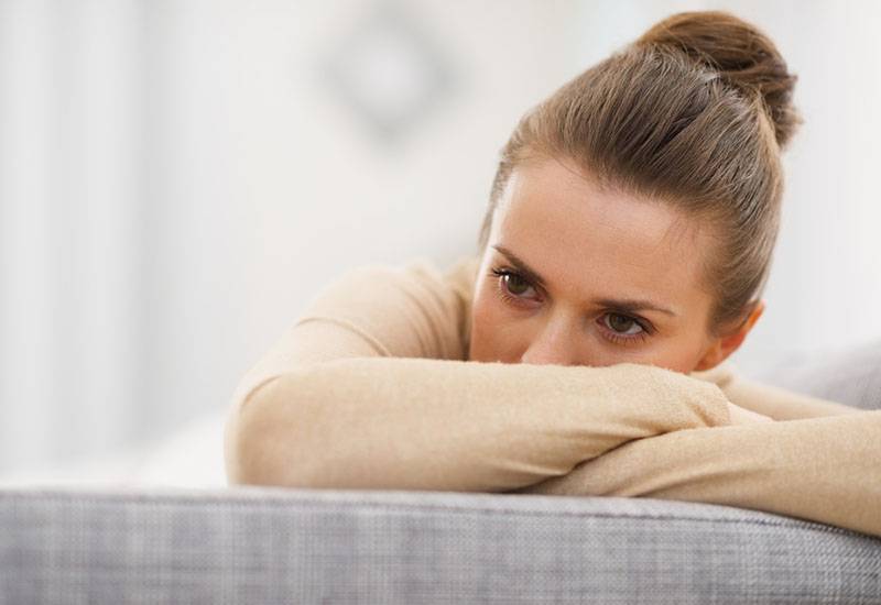 thoughtful woman with tied hair leaning on hands at home