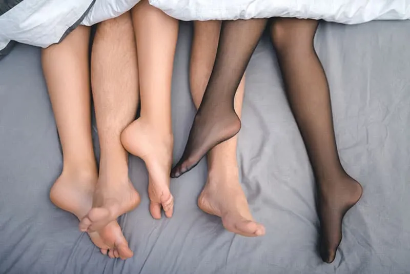 two woman's legs and one man's under blanket