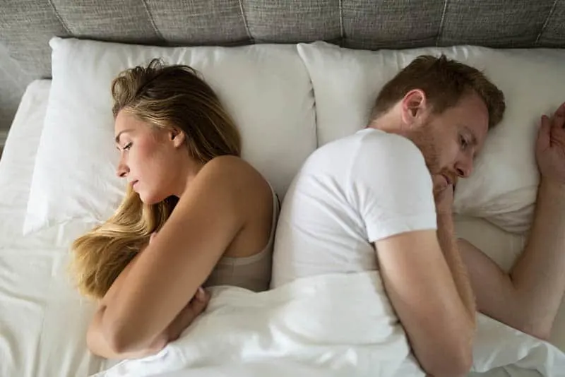 unhappy couple lying on bed back to back
