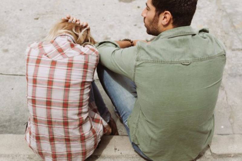 donna che si copre la testa con le mani mentre il suo uomo le sta accanto