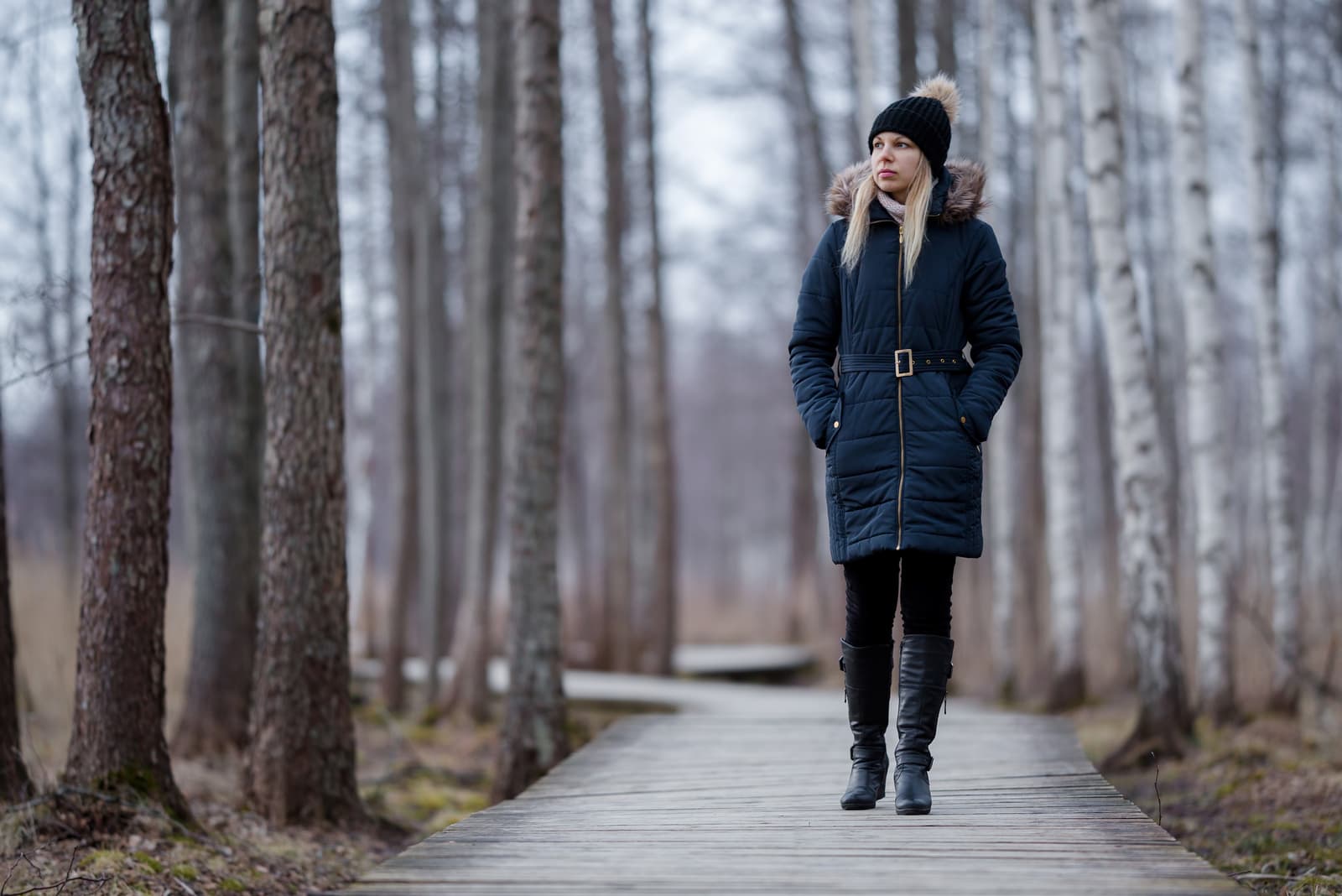 woman in dark warm clothes slowly walking on wooden trail at natural park
