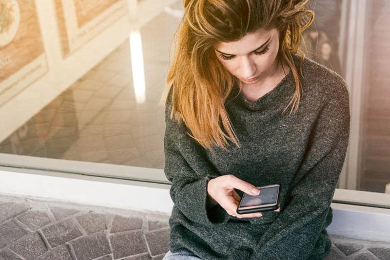 la donna abbassa lo sguardo e digita sul suo telefono