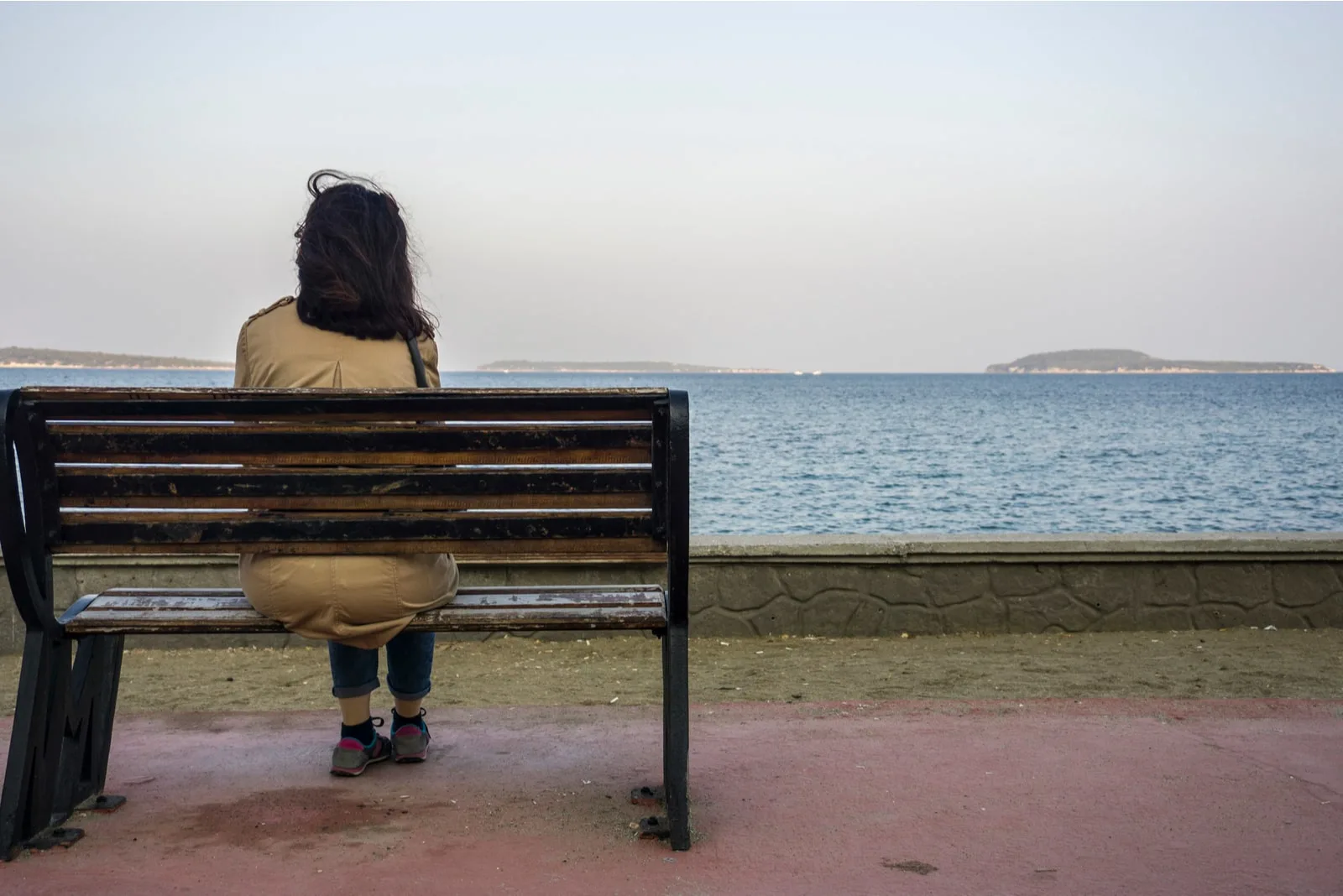 woman sit alone on bench, looking at distant sea 