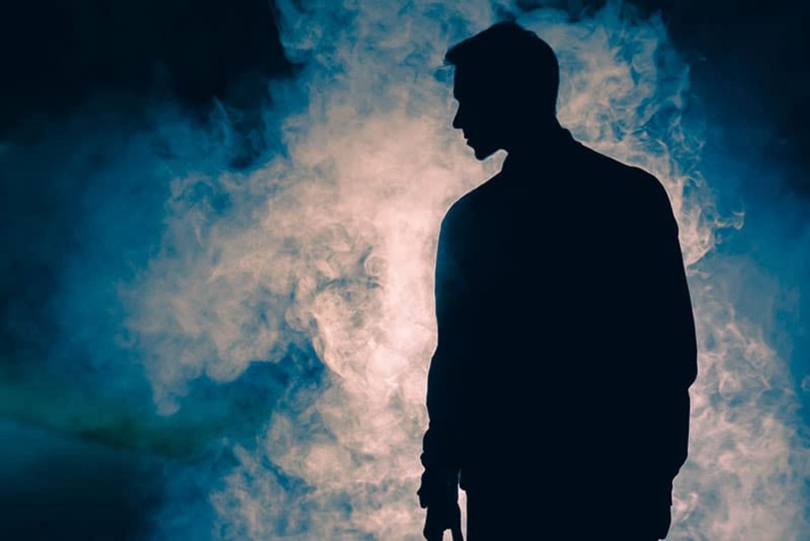 young man standing in darkness with smoke in front of him