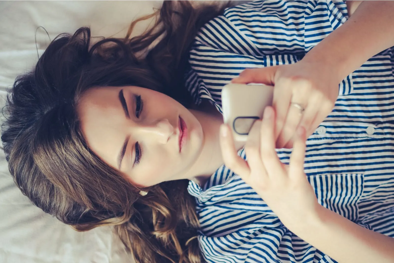 young woman lying in bed and texting on phone