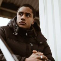 thoughtful man wearing black jacket and rings sitting outside