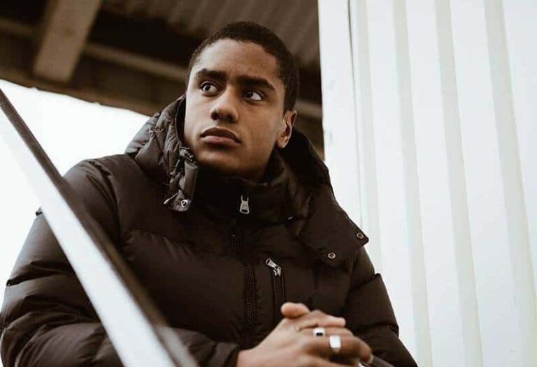 thoughtful man wearing black jacket and rings sitting outside