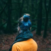 back view of woman with blue hair and wearing yellow sweatshirt in nature