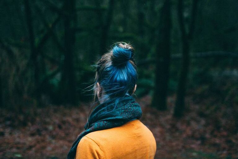 back view of woman with blue hair and wearing yellow sweatshirt in nature