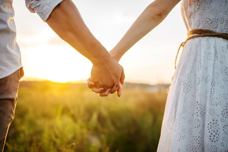 couple holding hands in green field