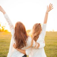 two girls having fun on a meadow at sunset