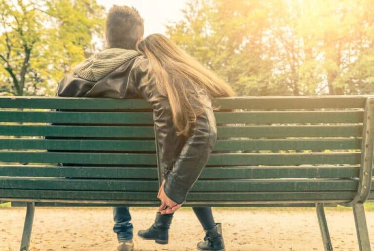 casal de mãos dadas e sentado num banco de jardim