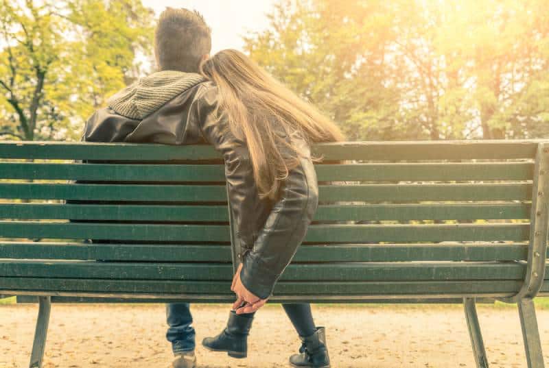 couple holding hands and sitting on a bench in park